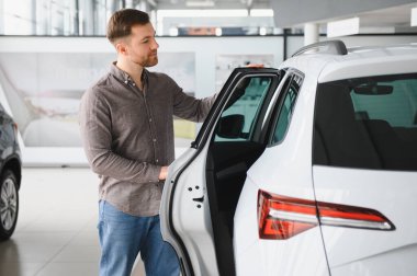 Müşteri galerideki yeni beyaz SUV 'u inceliyor, kapıyı açıyor ve içeriyi kontrol ediyor.