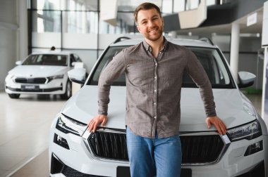 Yeni bir araç almanın verdiği heyecandan zevk alan, galeride gösterişli beyaz bir arabaya yaslanan mutlu bir adam.