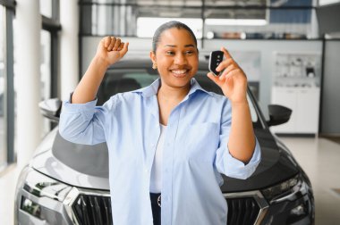 Neşeli bir galeride araba anahtarlarını tutarken yeni araba alımını kutlayan mutlu bir müşteri.