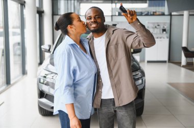 Heyecanlı çift yeni araba alımlarını kutluyor, öpüşüyor ve anahtarı bir araba galerisinde gösteriyor.