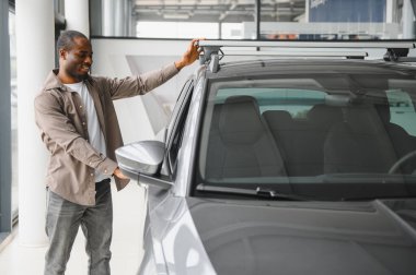 Yeni arabasının çatı rafını kontrol eden mutlu müşteri, modern bir galeride alışverişinin keyfini çıkarıyor.