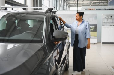 Afro-Amerikalı bir kadın galeride yeni bir arabanın çatısına nazikçe dokunuyor.