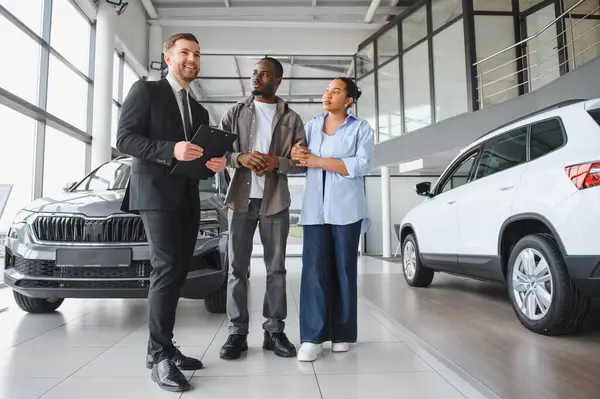 Araba satıcısı elinde yeni arabaları modern galeride Afro-Amerikan bir çifte sunuyor.