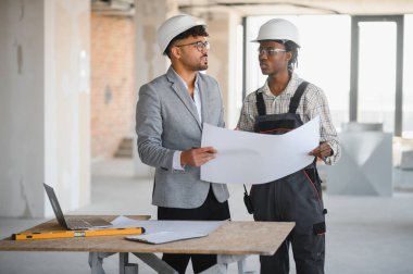 Mimar ve inşaatçı bir inşaat alanının planlarını tartışıyor. Mimarlık ve inşaat projelerinde takım çalışması ve işbirliği