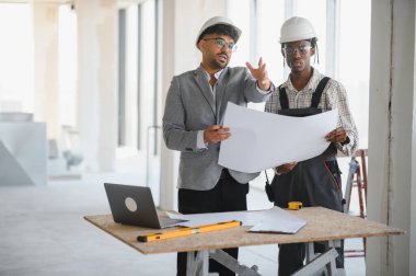 Mimar ve müteahhit, hareketli bir inşaat sahasında yapılan ortak bir toplantıda ayrıntılı bir planlar üzerine tartışmaya girişti.