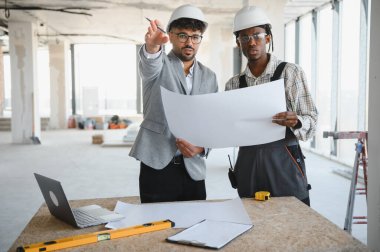 Mimarla planlar tartışılırken binanın içinde inşaat halindeki planlar tutuluyor, takım çalışması ve işbirliği vurgulanıyor