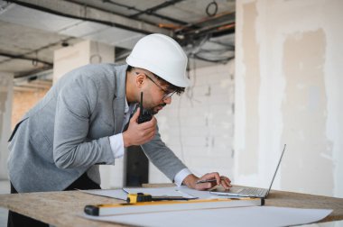 Arap mimar dizüstü bilgisayar ve telsiz kullanarak bir inşaat alanını yönetiyor.