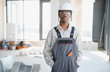 Genç Afro-Amerikan inşaat işçisi. İş tulumu, şapka ve koruyucu gözlük takıyor.
