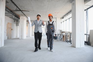 Mimarın elinde inşaat halindeki binayı gösteren planlar var. İnşaatçıların yürümesi ve gelişim hakkında konuşması için.