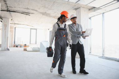 İnşaat halindeki bir binanın içinde yürüyen bir inşaatçıya dizüstü bilgisayardaki bilgileri gösteren mimar