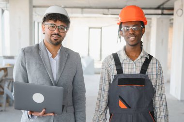 Arap mimar ve Afrikalı Amerikalı müteahhit bitmemiş bir binanın planlarını, takım çalışmasını ve inşaat alanındaki çeşitliliği tartışıyorlar.