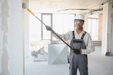 İnşaat işçisi inşaat halindeki patenle duvar boyuyor..