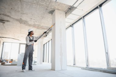 İnşaat işçisi inşaat halindeki patenle duvar boyuyor..