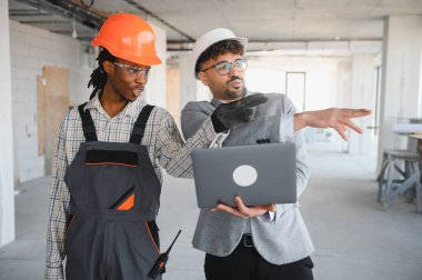 İnşaat alanında inşaatçıyla proje tartışırken dizüstü bilgisayar tutan ve bir şeyi işaret eden mimar