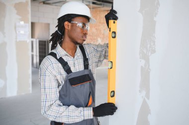 Genç Afro-Amerikan inşaatçı inşaat çalışmasında duvarın dikey görünmesini sağlamak için ruh seviyesini kullanıyor.