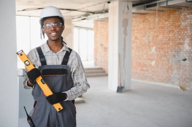 Genç Afro-Amerikan inşaat işçisi inşaat halindeki kameraya gülümsüyor.