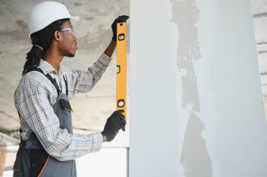 Genç Afrikalı Amerikalı inşaatçı inşaat sırasında pencere çerçevesinin dikey hizalanmasını sağlamak için ruh seviyesini kullanıyor