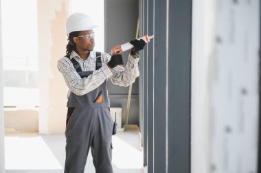 Afrikalı Amerikalı inşaat işçisi, düzgün yalıtım ve havalandırma sağlamak için inşaat alanındaki bir pencere çerçevesine dolgu macunu sürüyor.