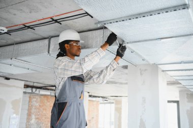 Afrika kökenli Amerikalı inşaat işçisi hareketli bir şantiyeye havalandırma sistemi kuruyor ve uygun hava akışını ve konforu sağlıyor.