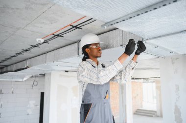 Güvenlik gözlüğü takan Afrikalı Amerikalı inşaat işçisi inşaat halindeki bir binaya havalandırma sistemi kuruyor.