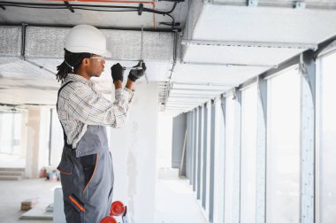 Afrika kökenli Amerikalı inşaat işçisi yoğun bir şantiyeye havalandırma sistemi kuruyor, kalite ve verimliliği sağlamaya odaklanıyor.