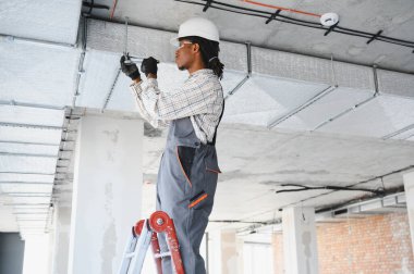 Afrikalı Amerikalı inşaat işçisi inşaat sahasına havalandırma sistemi kuruyor, merdiven üzerinde çalışıyor ve aletler kullanıyor.