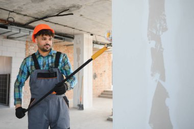 Turuncu kask takan inşaat işçisi, duvarlara alçı uyguluyor. İç mekanı ustalıkla geliştiriyor.