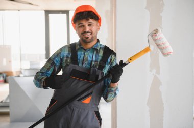 Duvarı boyamak için paten fırçası kullanan, inşaat alanında uzmanlık ve adanmışlık gösteren sert şapkalı bir Arap mühendis.