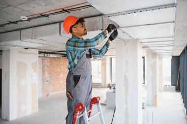 Merdivende çalışan elektrikçi inşaat halindeki bir binaya havalandırma sistemi kuruyor.