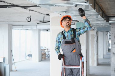 Elektrikçi merdiven üzerinde çalışıyor, inşaat halindeki bir binaya havalandırma sistemi kuruyor, uygun hava akışını ve verimliliği sağlıyor.