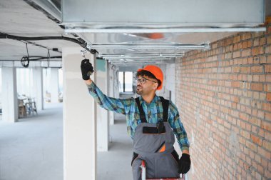 Arap mühendis inşaat alanına havalandırma sistemi kuruyor, tavanda turuncu bir kaskla çalışıyor.