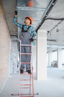 Güvenlik kaskı takan Arap mühendis inşaat sahasına havalandırma sistemi kuran metal merdiven üzerinde çalışıyor.