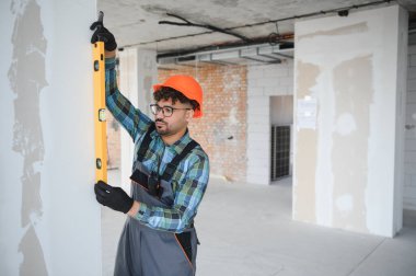 Odaklanmış mühendis titizlikle ruh seviyesini kullanır, hareketli bir inşaat alanındaki duvarın dikey hizalanmasını sağlar.