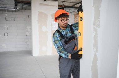 Ev yenileme projesi sırasında bir duvarın dikey hizalanmasını sağlamak için ruh seviyesini kullanan Arap inşaatçı