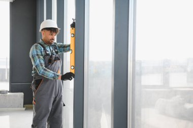 Modern bir inşaat sahasının inşaatını denetlerken bir yandan da bir pencere çerçevesinin ruh seviyesini kontrol eden Arap mühendis.