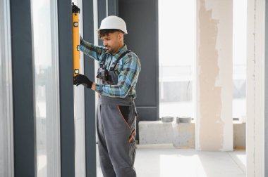 Arap müteahhit, hareketli bir inşaat sahasındaki ruh seviyesiyle bir pencere çerçevesinin dikeyliğini kontrol ederek kesin ölçümler yapıyor.