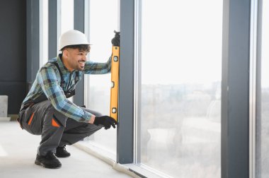 Arap inşaat işçisi, bina yenilenmesi veya inşaatı sırasında pencere çerçevesini ruh seviyesiyle kontrol ediyor, kesin hizalama ve yapısal bütünlüğü sağlıyor