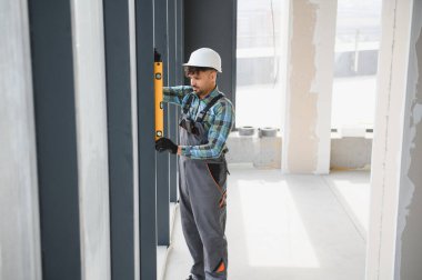 Pencere çerçevesinde ruh seviyesini kullanan inşaat işçisi.