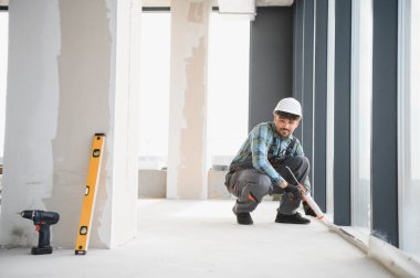 İnşaat işçisi, yoğun bir inşaat alanında çalışırken pencere çerçevesine dolgu macunu sürerek kalite ve güvenliği sağlıyordu.