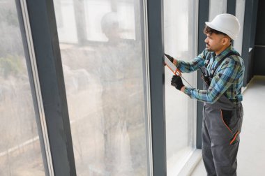 İnşaat işçisi, pencere çerçevesine bir kabartma tabancasıyla dolgu macunu sürüyor. Binanın içine tam ve güvenli bir şekilde sığmasını sağlıyor.