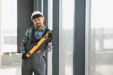 Pencere çerçevesinde ruh seviyesini kullanan inşaat işçisi.