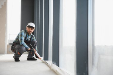 İnşaat işçisi, inşaat halindeki modern binanın pencere çerçevesine silikon dolgu maddesi kullanıyor.