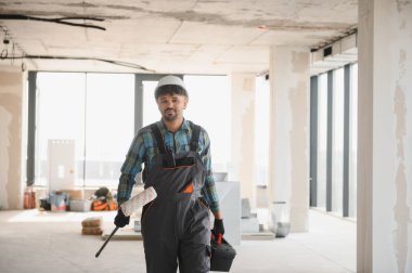 Arap mühendis başlık takıyor ve boya silindiri tutuyor ve bina içinde inşaat halinde yürüyor.