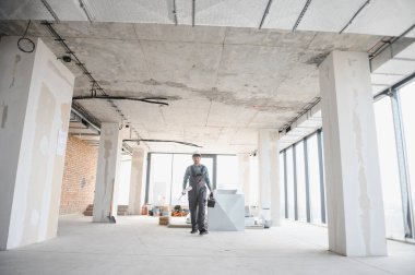 İnşaat sırasında elinde planlar ve aletlerle büyük, tamamlanmamış bir binada yürüyen mühendis.