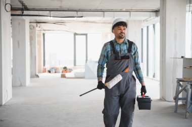 Arap inşaat işçisi inşaat halindeki bir binanın içinde araç kutusu ve boya silindiri taşıyordu.