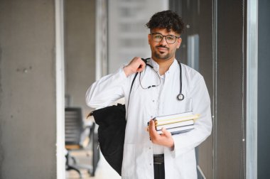 Üniversite koridorunda kitap ve sırt çantası taşıyan kendinden emin bir tıp öğrencisinin portresi.