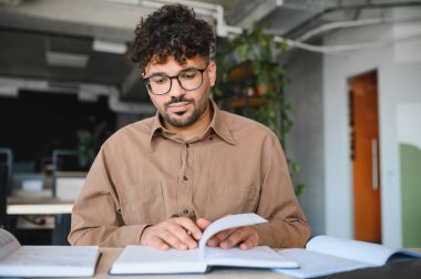 Genç Arap öğrenci, sakin ve parlak bir atmosferle çevrili modern bir üniversite kütüphanesinde sınavlara hazırlanırken ders kitaplarına konsantre oluyor.