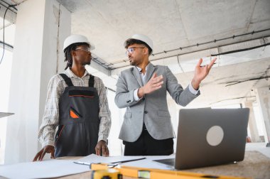 Çalışan bir inşaat sahasında yapılan ortak bir toplantıda inşaatçıya proje detaylarını açıklayan mimar