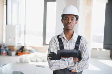 Genç Afro-Amerikan inşaat işçisi yoğun bir inşaat sahasında dikilirken kendine güvenerek silah doğrultuyor ve mesleğiyle gurur duyuyor.