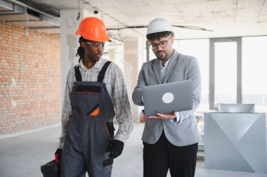 İnşaat gezisi sırasında inşa edilecek bir dizüstü bilgisayarın üzerinde bina planlarını sunan mimar, işbirliğini teşvik ve proje ilerlemesini güvence altına alıyor